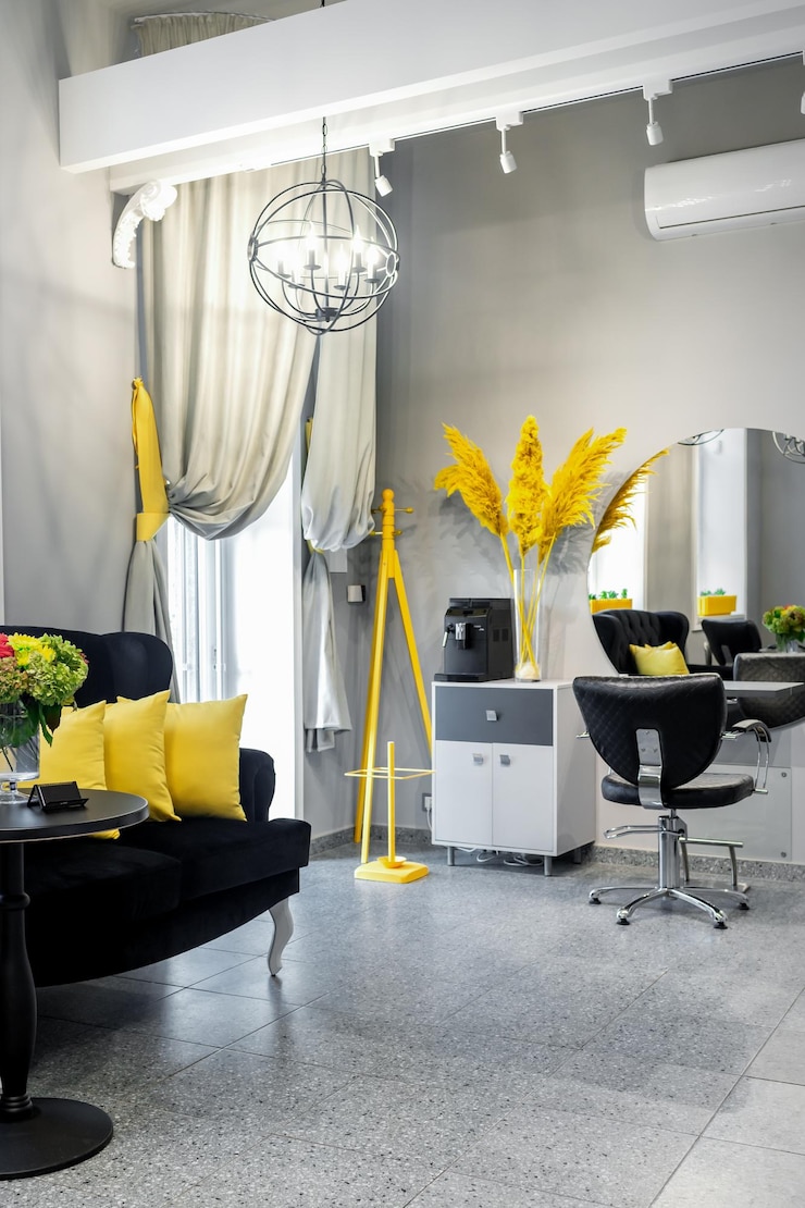 Zdjęcie nowoczesny mały jasny salon fryzjerski i kosmetyczny w czarno-żółtych kolorach z szarymi ścianami i podłogą oraz czarną sofą z żółtymi poduszkami