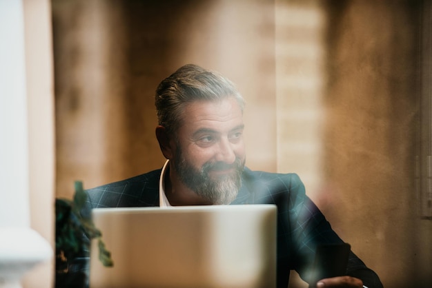 Nowoczesny starszy biznesmen siedzący w kawiarni i używający laptopa i smartfona