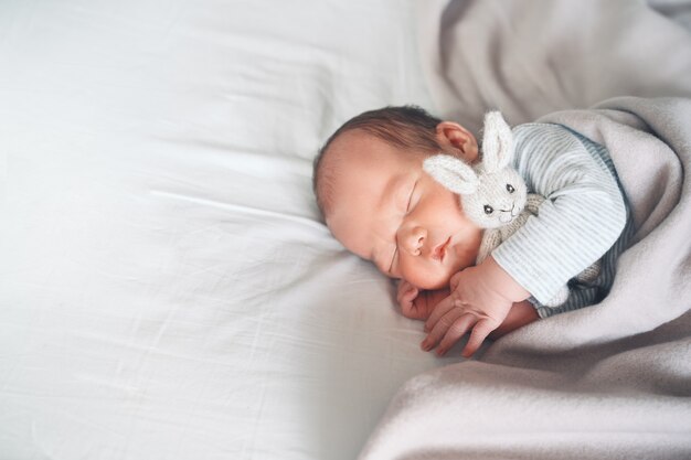 nowonarodzone dziecko chłopiec w wieku jednego tygodnia śpi spokojnie z uroczą miękką zabawką w łóżeczku w tkaninowym tle