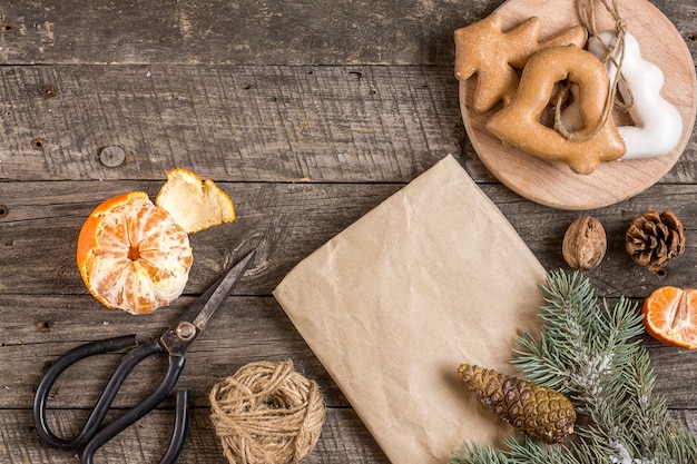 Noworoczna kompozycja. Papier do pakowania prezentów, nożyczki, gałąź świerkowa i świąteczne pierniki na drewnianym tle. Boże Narodzenie, zima, koncepcja nowego roku. Płaski świeckich, widok z góry.