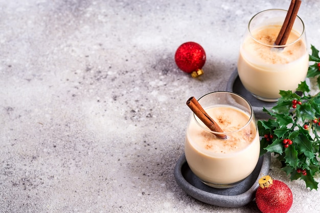 Noworoczny lub świąteczny koktajl ajerkoniakowy, gorący zimowy lub jesienny napój z cynamonem i gałką muszkatołową w szklance na jasnym kamieniu, świąteczna dekoracja