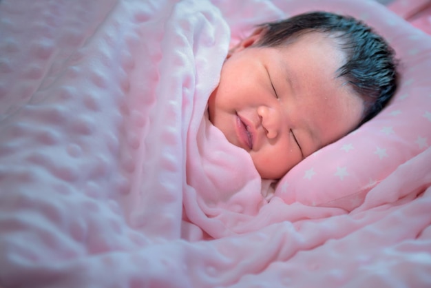 Noworodek Azjatka ma 7 dni jest uśmiechnięta i śpi pod różowym kocykiem