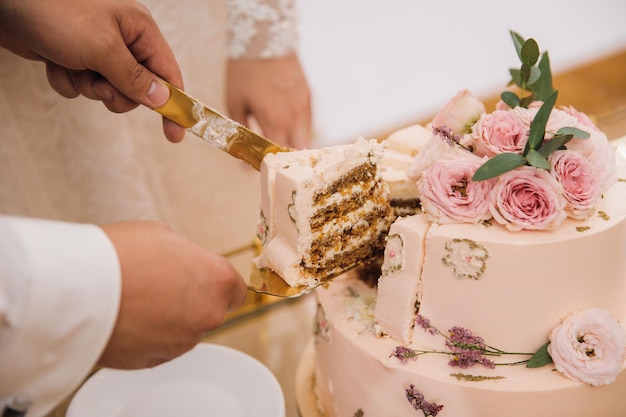 Nowożeńcy kroją kawałek tortu weselnego ozdobionego pąkami róż