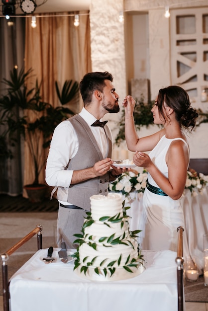 Nowożeńcy radośnie kroją, śmieją się i smakują tort weselny