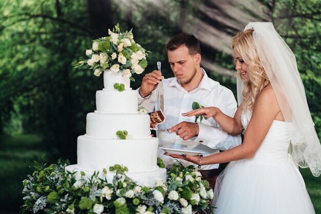 Nowożeńcy radośnie kroją, śmieją się i smakują tort weselny