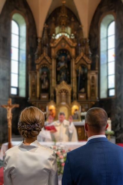 Zdjęcie nowożeńcy stojący przed ołtarzem ksiądz udzielający błogosławieństwa