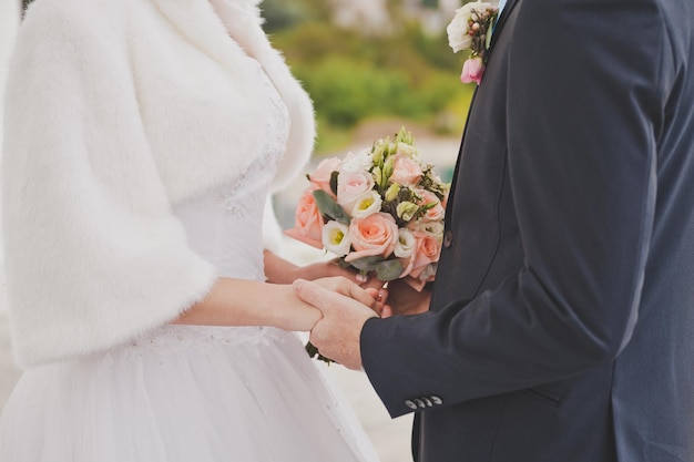 Zdjęcie nowożeńcy trzymają się za ręce za bukiet z obu stron 790
