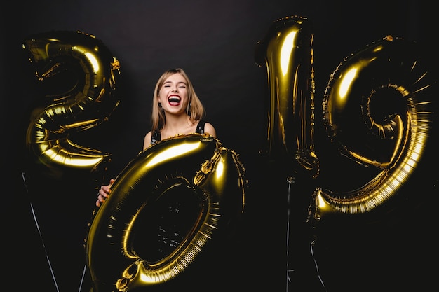 Nowy Rok. Kobieta Z Balonami Świętuje Przy Przyjęciem. Portret pięknej uśmiechniętej dziewczyny w błyszczącej sukience rzucanie konfetti, zabawy z balonami złota 2019 na tle. Wysoka rozdzielczość.