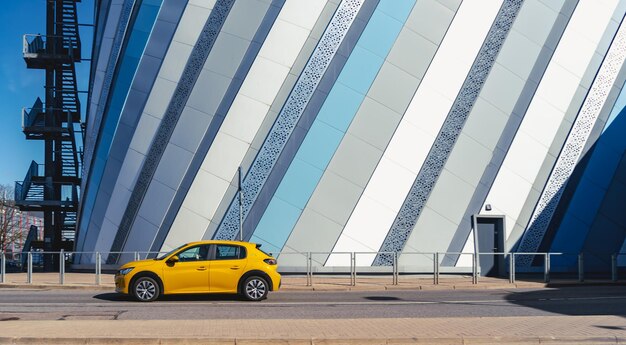 Nowy żółty hatchback przejeżdża w słoneczny dzień obok nowoczesnego budynku Żółty samochód