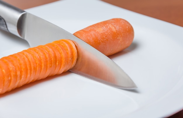 Nóż do krojenia marchewki na białym talerzu nad stołem
