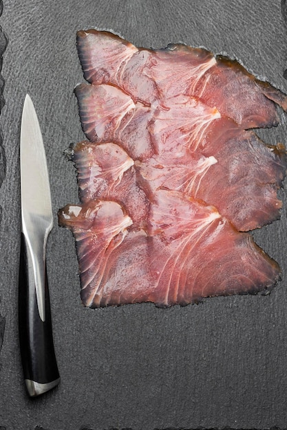 Nóż kuchenny i cienkie plasterki tuńczyka na kamiennej desce