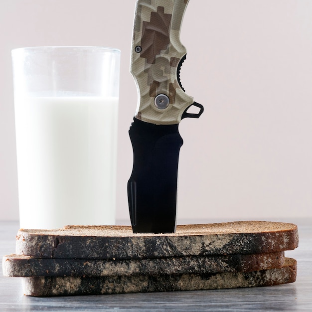 Zdjęcie nóż utknął w kawałkach chleba, a obok niego szklanka mleka