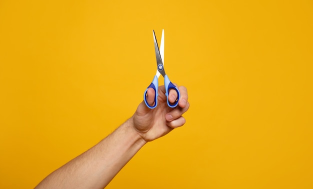 Nożyce. Close-up zdjęcie dłoni trzymającej nożyczki na żółtym tle. Koncepcja remontu domu.