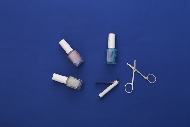 Nożyczki do manicure, butelka lakieru do paznokci i maszynki do strzyżenia na klasycznym niebieskim kolorze. Pojęcie piękna. Pielęgnacja paznokci