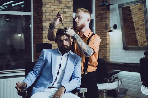 Nożyczki fryzjerskie i brzytwa Fryzjer golący brodatego mężczyznę w zakładzie fryzjerskim Brodaty mężczyzna strzyżony przez fryzjera i siedzący na krześle u fryzjera