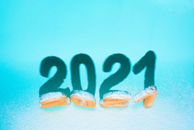 Numer 2021 ciasteczek imbirowych posypanych cukrem pudrem, twarde cienie na niebieskiej ścianie. świąteczna ściana nowego roku, szablon kart okolicznościowych. projekt koncepcyjny, miejsce na tekst.