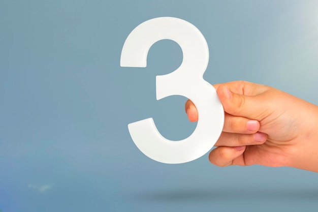 Numer trzy w ręku trzymając biały numer na niebieskim tle z koncepcją przestrzeni kopii z odrętwieniem