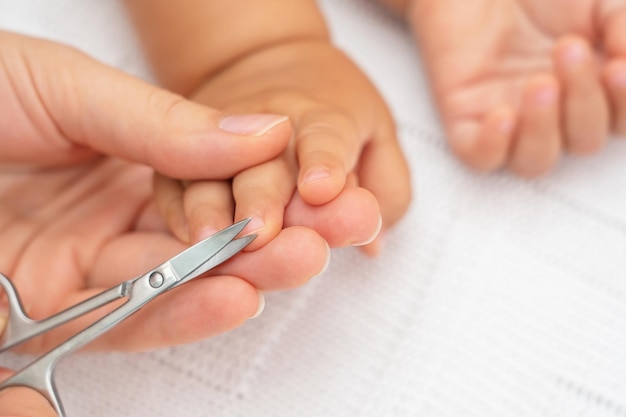 Obcinanie paznokci dziecka. Dłoń z nożyczkami obcina paznokcie śpiącego dziecka. Selektywne skupienie