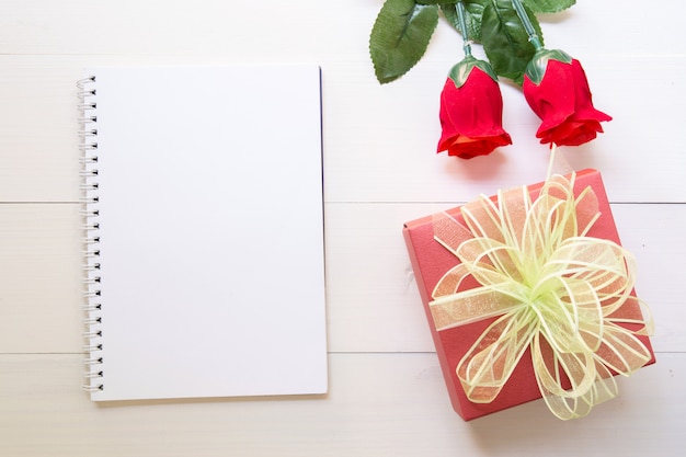 Obecny czerwony kwiat róży i notatnik i pudełko z miejsca na kopię na drewnianym stole