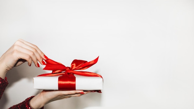 Obecny prezent Dzień kobiety powitanie Szczęśliwe wakacje Tło reklamowe Elegancka kobieca ręka trzymająca świąteczne pudełko czerwona wstążka na białym tle biała kopia miejsca
