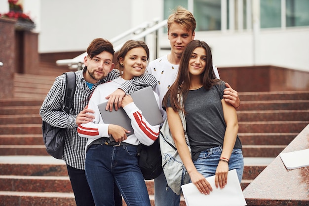 Obejmując się nawzajem. Grupa młodych studentów w ubraniu w pobliżu uniwersytetu w ciągu dnia.