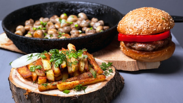 Obfity, rustykalny lunch. frytki burger i pieczarki pieczarki pieczone w żeliwie na leśnych drewnianych podstawkach.