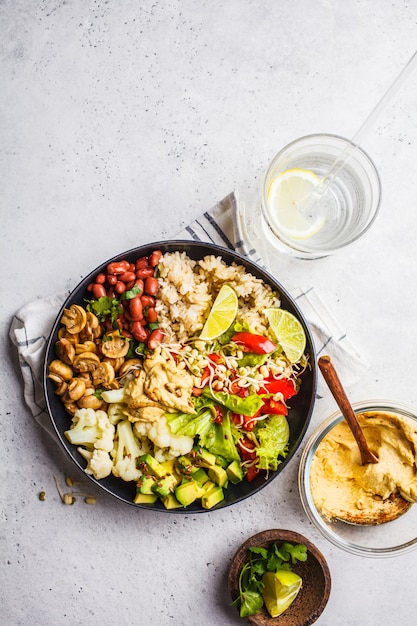 Obiad wegetariański. Brown ryż z pieczarkami, fasolami, sałatką i hummus w czarnym talerzu, czysty eatind.