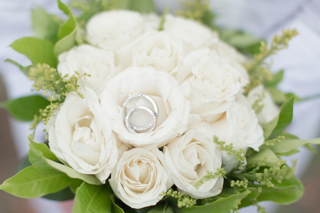 Zdjęcie obrączki ślubne z bukietem kwiatów białej róży.