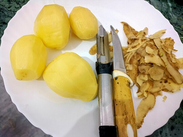 Zdjęcie obrane ziemniaki z nożem i skórką na białym talerzu