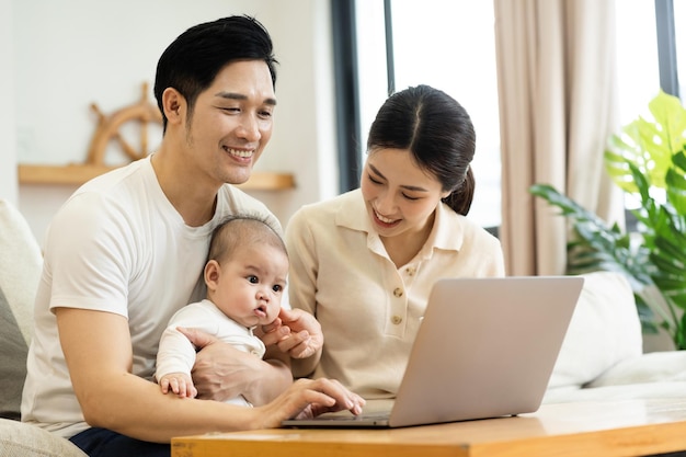 Obraz azjatyckiej rodziny z dzieckiem siedzącym na kanapie za pomocą laptopa