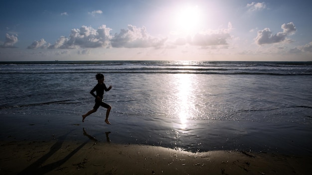 Zdjęcie obraz boczny sylwetki chłopca biegającego po plaży na tle nieba