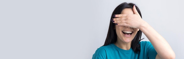Obraz brunetka nastolatka zasłaniając twarz rękami i zaglądając przez palce.