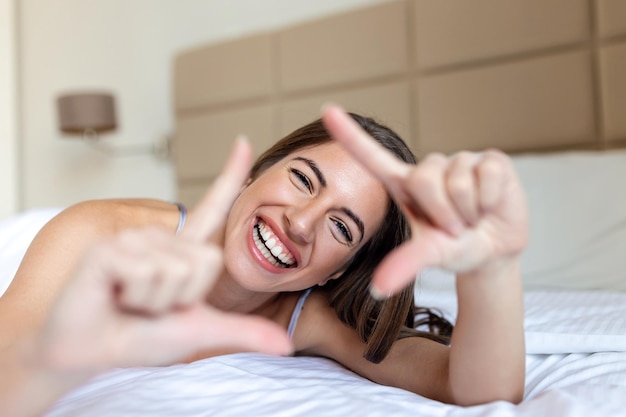 Obraz kobiety wykonującej znak ramki na zdjęcia palcami podczas leżenia w łóżku