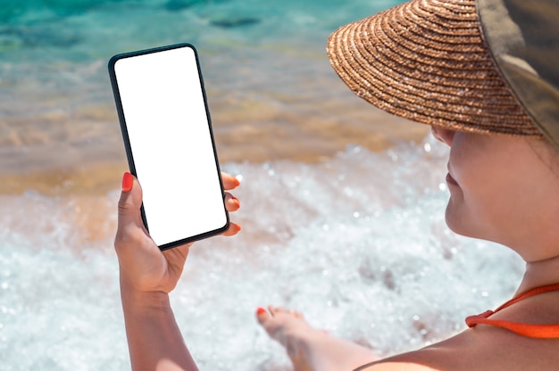 Obraz makiety. ręka trzyma i pokazuje modren inteligentny telefon komórkowy na plaży