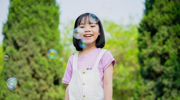 Obraz małej azjatyckiej dziewczynki bawiącej się bańkami mydlanymi w parku