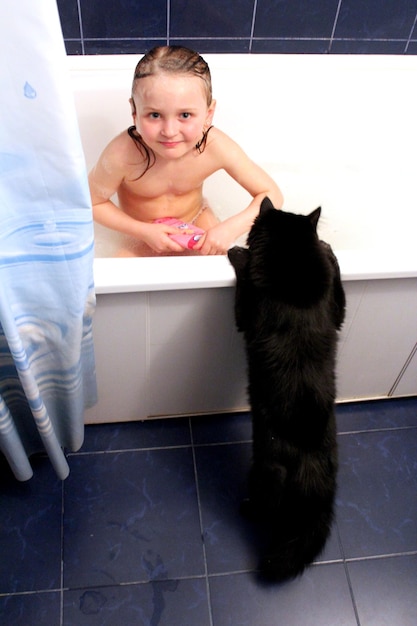 Obraz małej dziewczynki biorącej kąpiel z ciekawym czarnym kotem