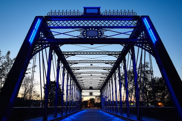 Obraz metalowego mostu świeci na niebiesko, gdy jest podświetlany przez zachodzące słońce