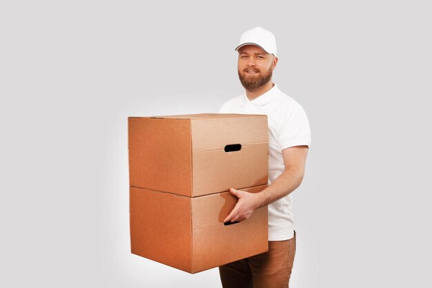 Obraz młodego dostawcy w białym mundurze trzymającego dwa duże pudełka i patrzącego w kamerę na szarym tle