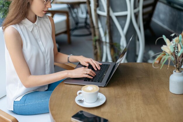 Obraz młodej kobiety pracującej na laptopie siedzącej przy stoliku kawowym