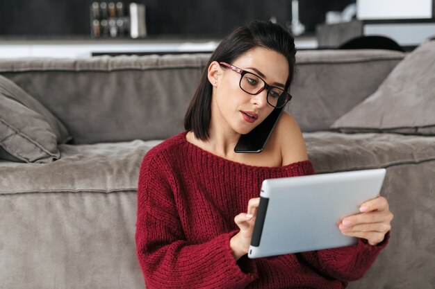 Obraz niesamowitej kobiety w domu w pobliżu sofy przy użyciu komputera typu tablet.