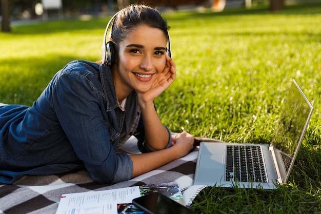 Obraz niesamowitej pięknej młodej kobiety studentki w parku przy użyciu komputera przenośnego słuchania muzyki w słuchawkach.