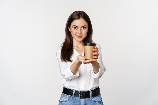 Obraz nowoczesnej kobiety w biurze, trzymającej filiżankę kawy na wynos i uśmiechniętej, stojącej na białym tle...