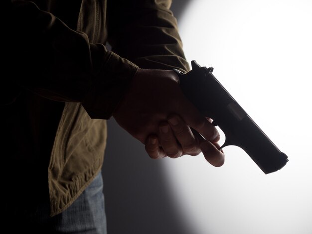 Obraz o wysokim kontraście przedstawiający mężczyznę trzymającego broń na jasno oświetlonym tle