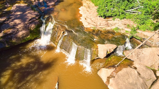 Obraz patrzenia w dół na wodospady nad głazem z brązowymi, omszałymi skałami i brązową wodą