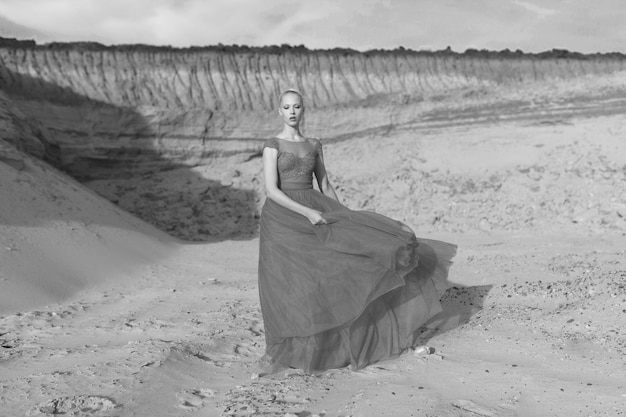 Obraz pełnej długości blond młoda kobieta w czerwonej sukience macha z latającego materiału na tle piasków.