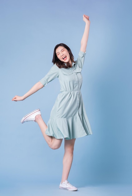 Obraz pełnej długości młodej azjatyckiej kobiety noszącej sukienkę na niebieskim tle