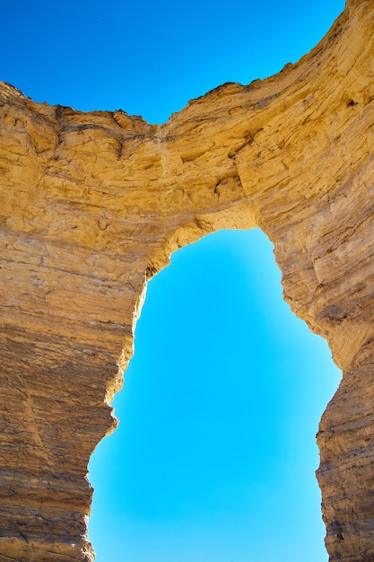 Obraz pionowego otwartego naturalnego łuku przecinającego biały kamień na tle błękitnego nieba