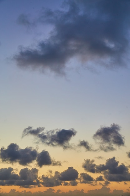 Obraz pionowy małych ciemnych chmur na tle stonowanych kolorów zachodu słońca
