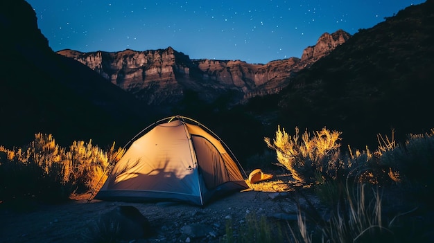 Obraz pokazuje samotny namiot w rozległym i nierównym górskim krajobrazie namiot jest oświetlony od wewnątrz nocne niebo jest czyste i gwiezdne