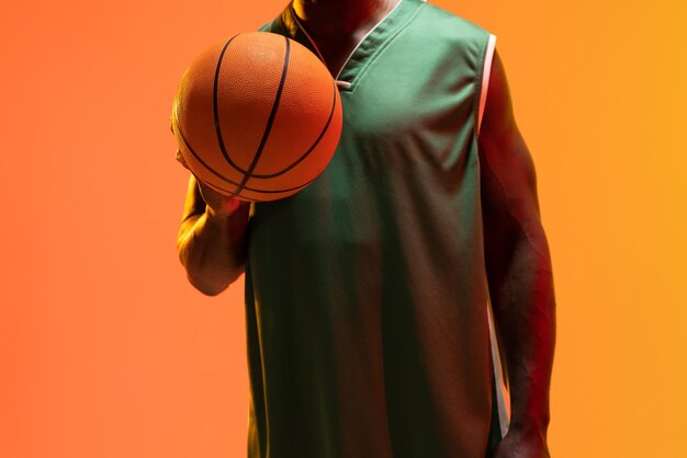 Obraz przedstawiający brzuch Afroamerykanina koszykarza grającego w koszykówkę na neonowym pomarańczowym tle. Koncepcja sportu i konkurencji.